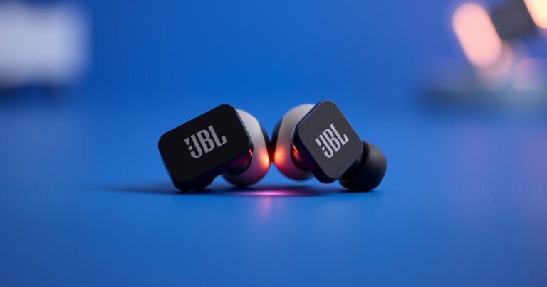 A close-up view of sleek JBL earbuds resting on a vibrant blue background, surrounded by glowing sound waves. The earbuds are partially open, showcasing their modern design, while subtle motion lines indicate connectivity. In the background, soft, blurred tech elements hint at wireless technology, evoking a sense of innovation and convenience.