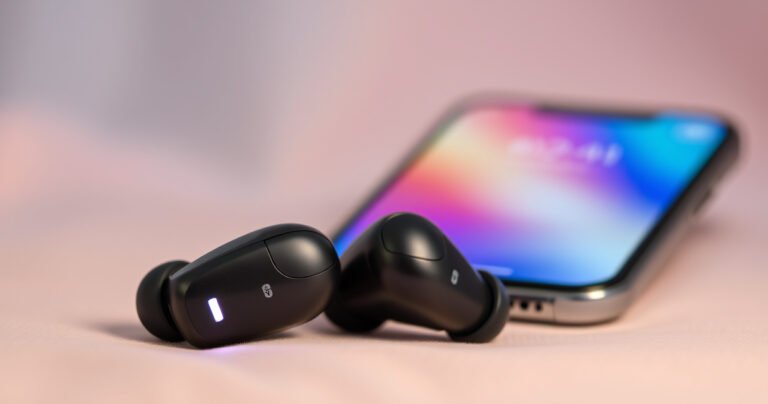 A close-up of two sleek wireless earbuds resting on a soft, blurred background of pastel colors, with gentle light reflecting off their glossy surfaces. One earbud is slightly tilted, revealing a tiny LED light, while a smartphone displays a vibrant setup screen, emphasizing a seamless pairing experience.