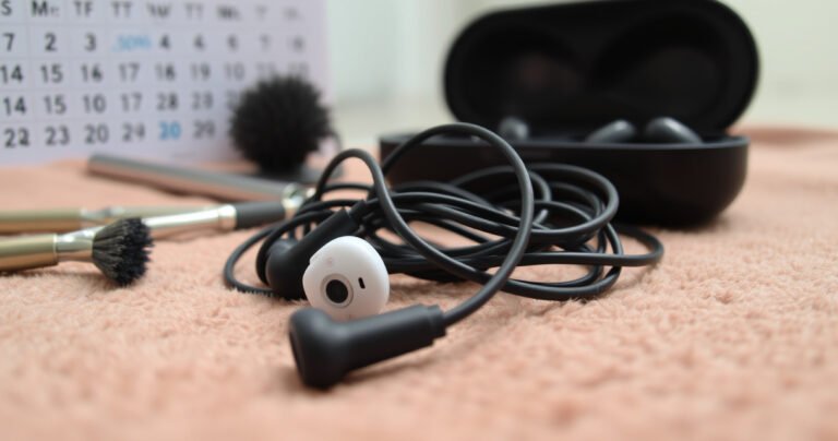 A close-up of a pair of worn, tangled earbuds resting on a soft, cozy fabric, surrounded by small tools like a cleaning brush and a charging case. In the background, a subtle calendar with marked dates symbolizes time, while soft, natural light creates an inviting atmosphere, hinting at care and longevity.